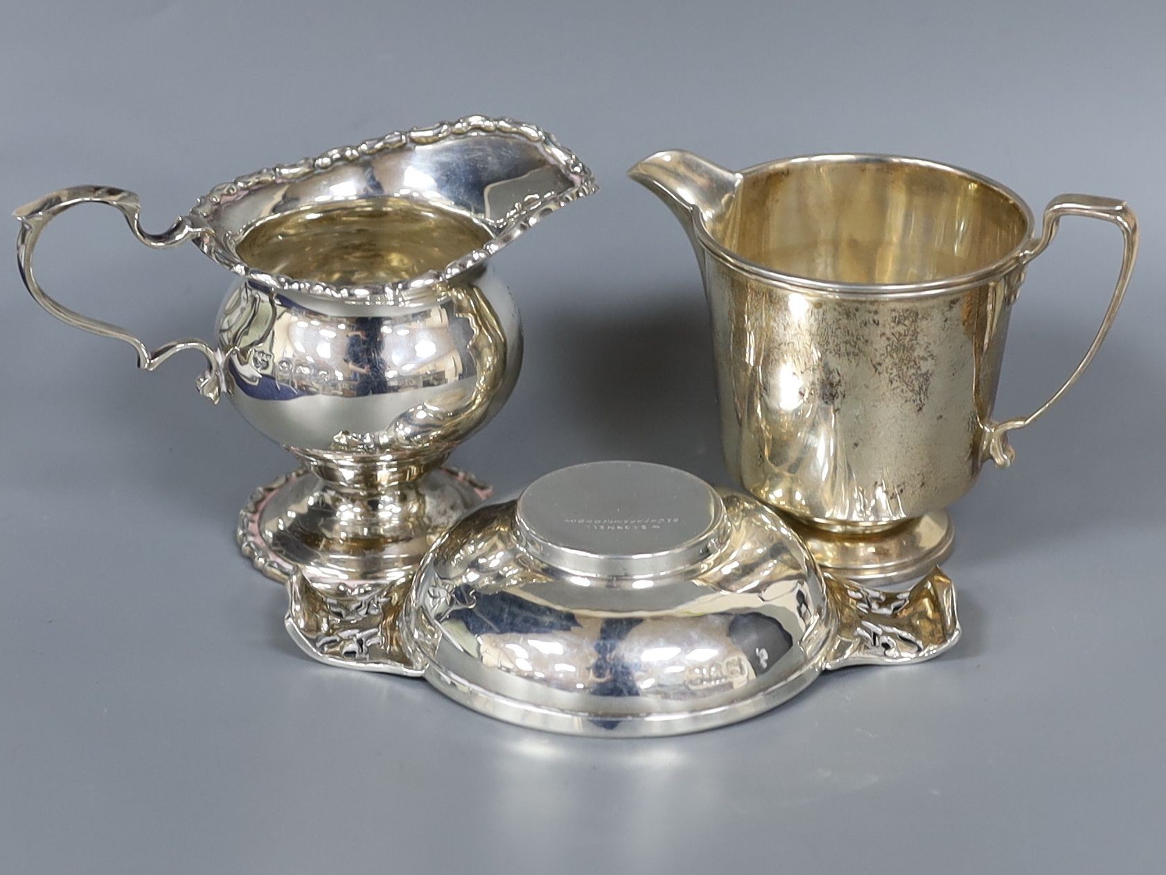 A late Victorian Art Nouveau small silver two handled dish, by W.G Connell, London, 1900, 12cm and two silver cream jugs, 7oz